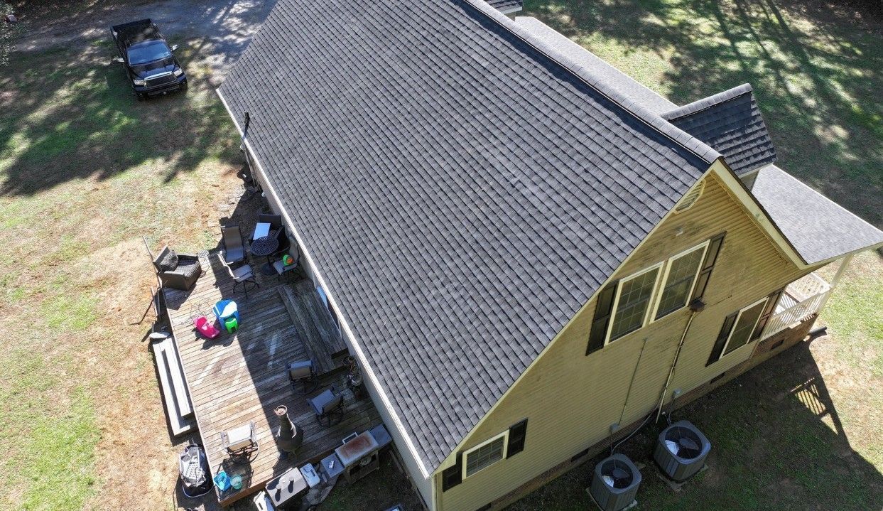 Aerial view of a house with a dark gray roof and a wooden deck. A black truck is parked nearby.