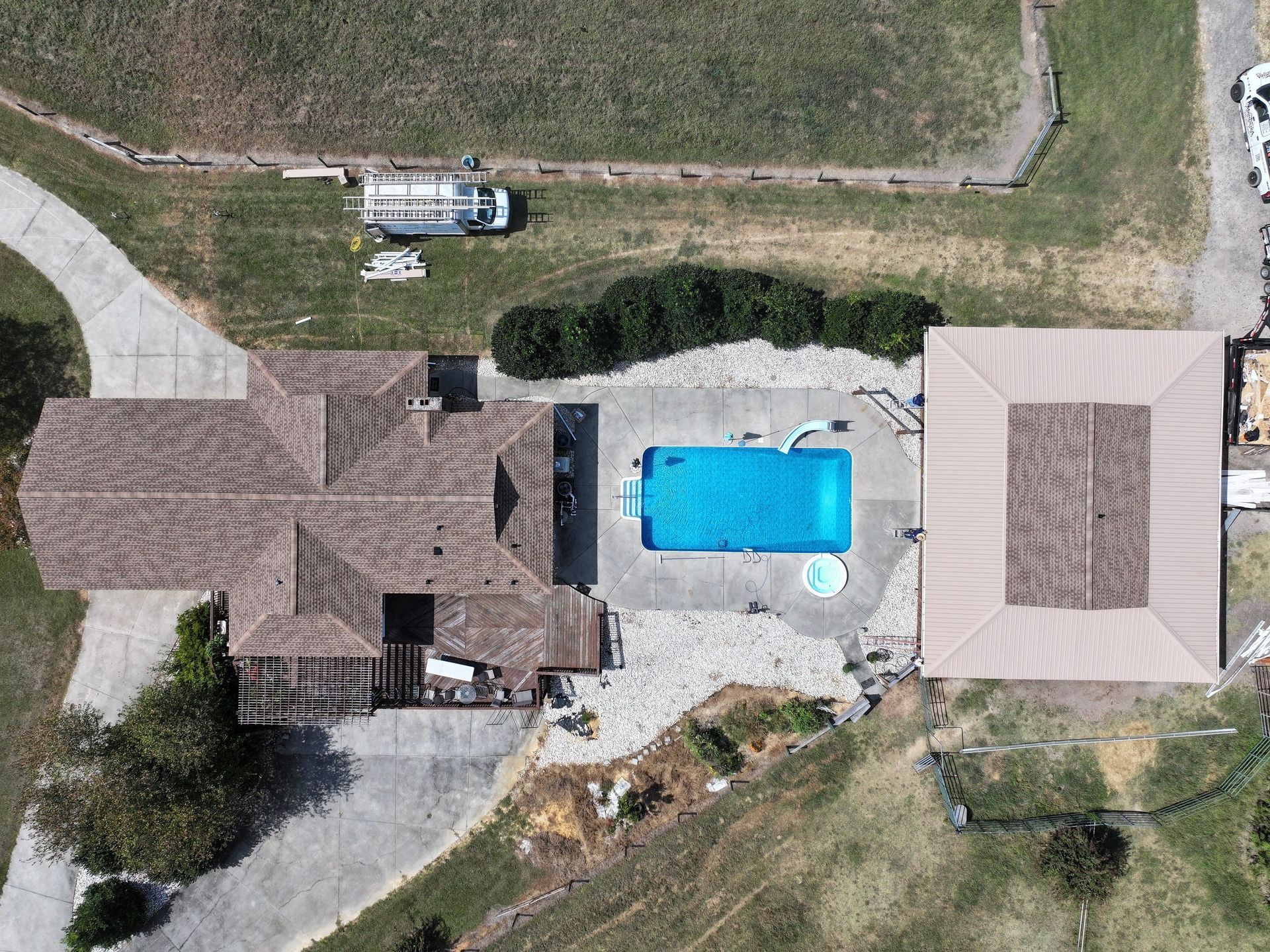 Aerial view of a house with a pool. The home is brown with a concrete driveway and a pool with blue water.