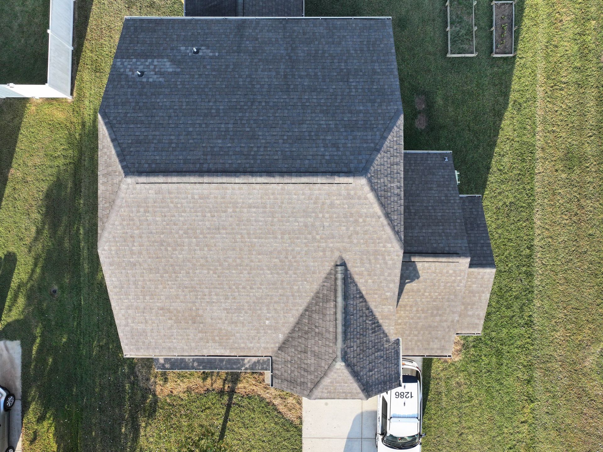 Overhead view of a house with a gray roof and a white car in the driveway on a sunny day.