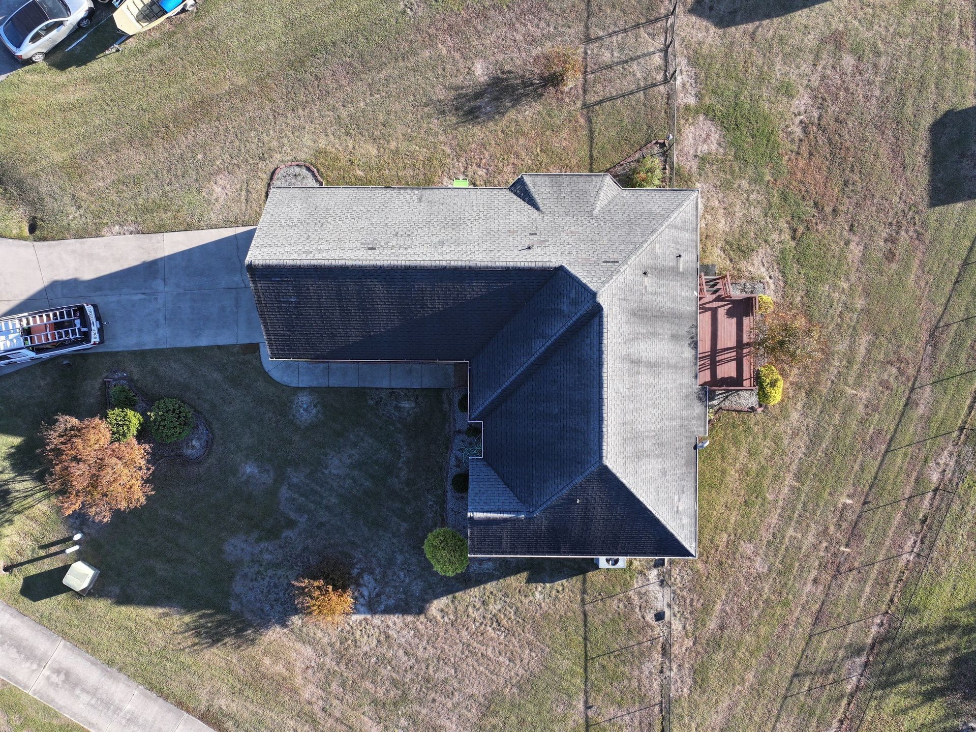 Overhead view of a house with a dark roof and a driveway, surrounded by brown grass and some trees.