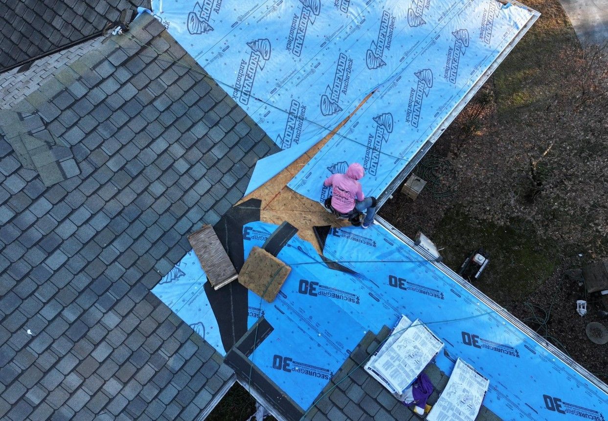 Roofer in pink jacket on a roof, installing underlayment on a section.