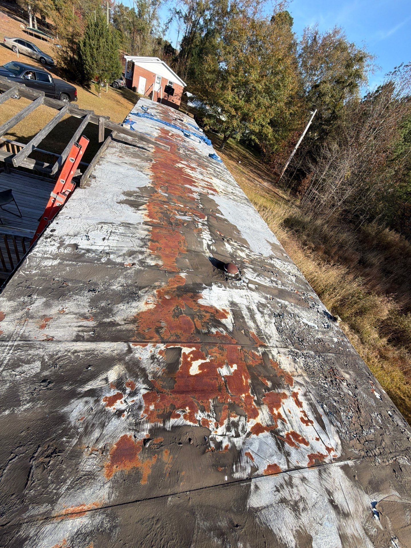 Weathered train car roof with peeling paint and a small building in the background.