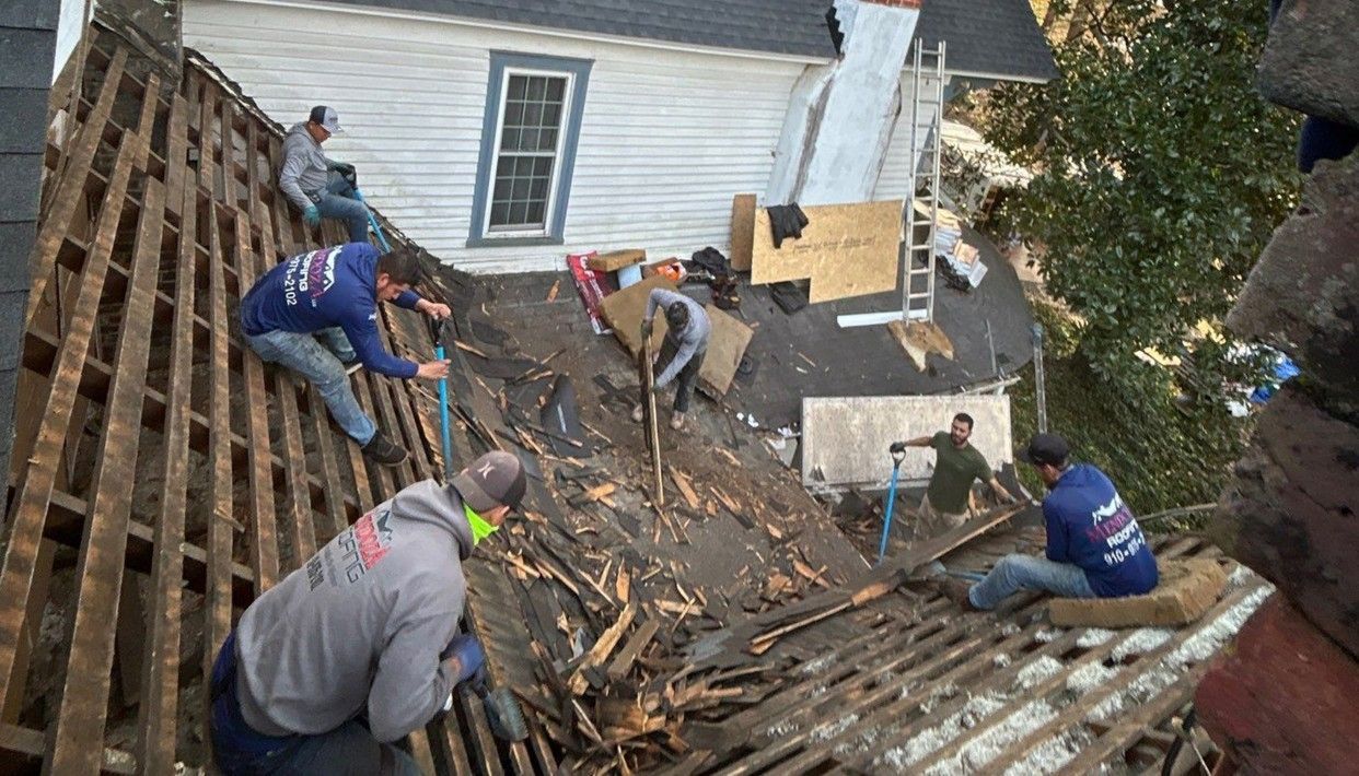 Workers removing old roofing material from a house. Several workers on the roof using tools.