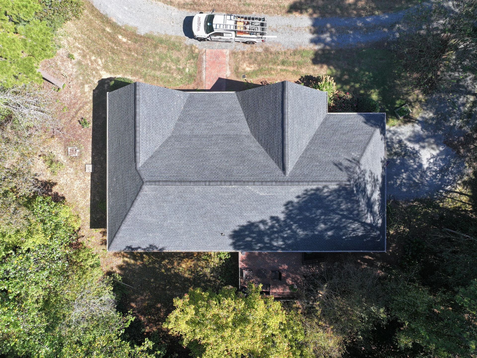 Overhead view of a house with a gray shingle roof, surrounded by trees. A truck is parked in the driveway.