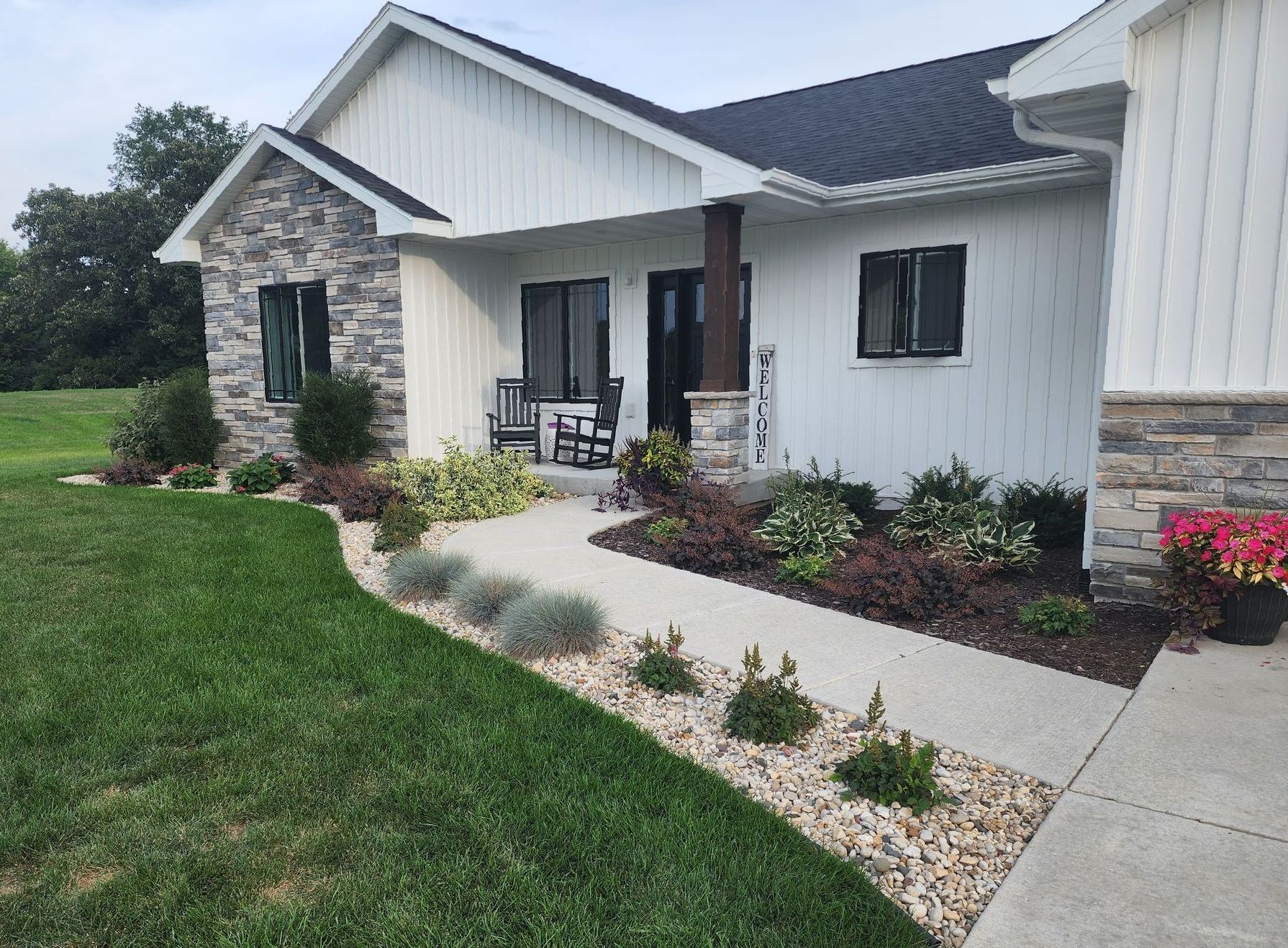A white house with a rocking chair on the porch and a walkway leading to it.