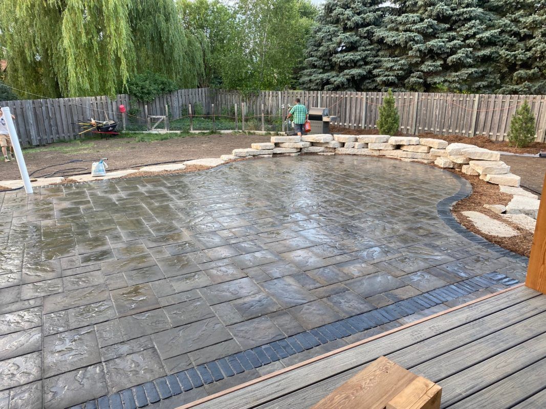 A man is standing in the middle of a patio in a backyard.