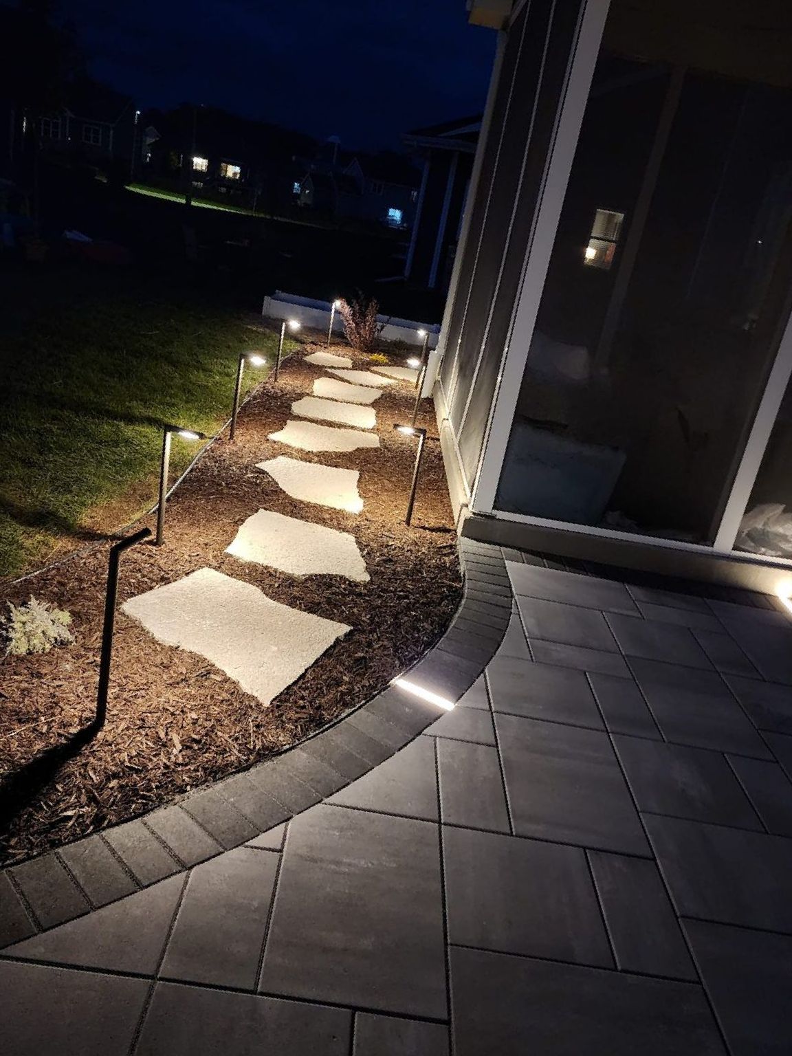 A patio with a walkway leading to a house at night.