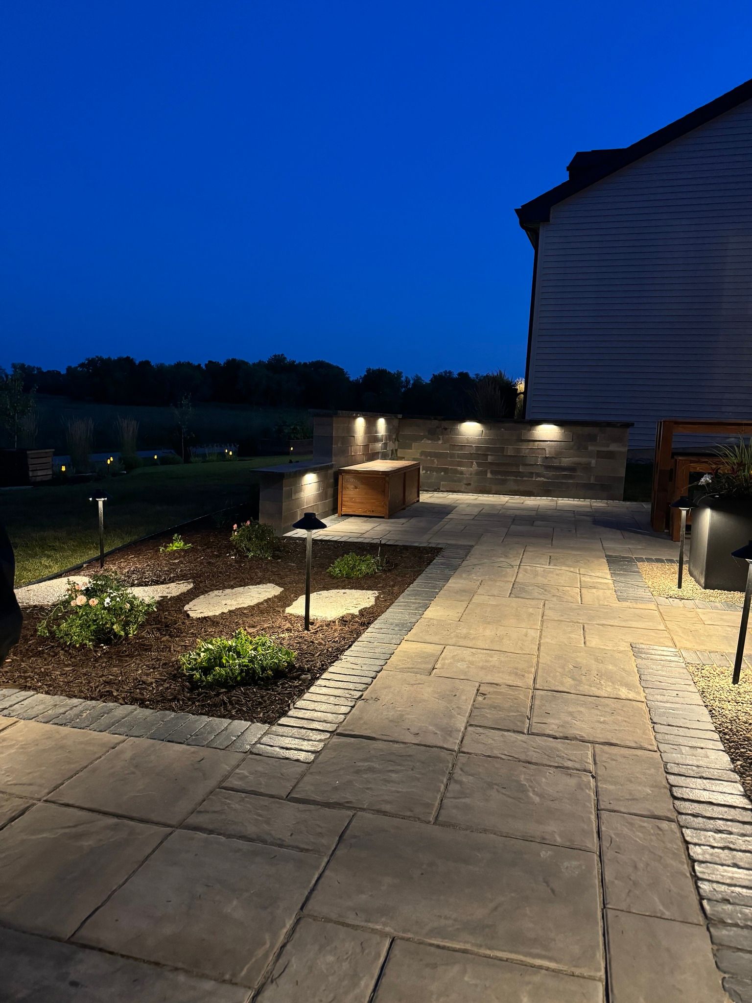 A patio is lit up at night with a house in the background.