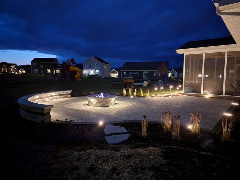 A patio with a fire pit and a screened in porch at night.