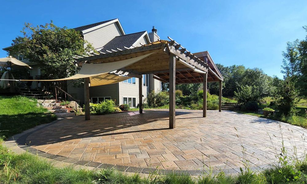 A large patio with a pergola and a house in the background.