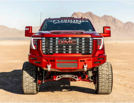 A custom red GMC heavy-duty truck with a large front bumper and lifted suspension parked in a desert landscape.
