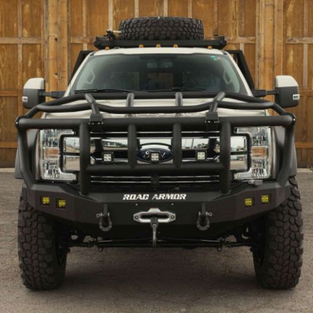 A white Ford pickup truck with a large black Road Armor brush guard, winch, off-road tires, and a roof-mounted spare tire.