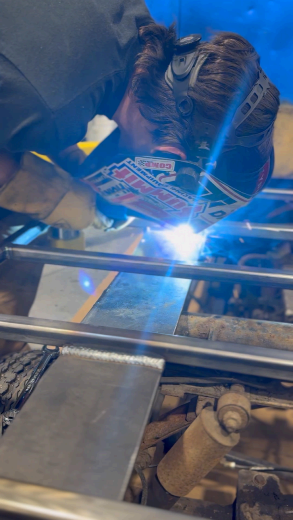 A person wearing a welding helmet and protective gloves uses a welding torch to join metal pieces in a workshop.