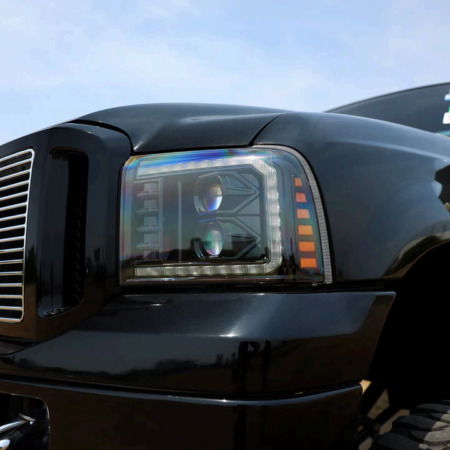 A close-up of a black truck's custom headlight, featuring dual projector lenses, LED strips, and amber turn signals.