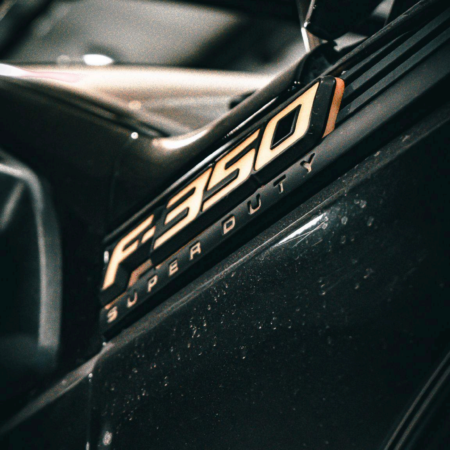 Close-up of a black Ford F-350 Super Duty emblem with gold lettering on a vehicle fender.