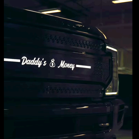 A close-up of a black truck grille featuring a white decal that says 