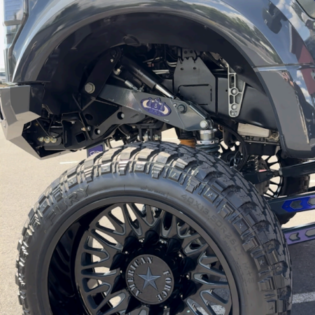 A close-up view of a truck's lifted suspension, large off-road tire, and an American Force wheel.