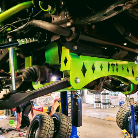 A neon green FTS suspension lift kit installed on the undercarriage of a truck in a repair shop.