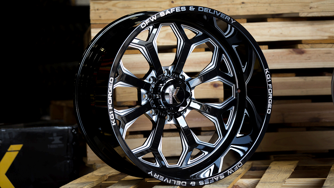 A polished, black and chrome multi-spoke truck wheel displayed on wooden pallets in a workshop.
