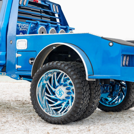 A custom blue flatbed truck with large, intricate blue and chrome wheels parked on a white, snowy surface.