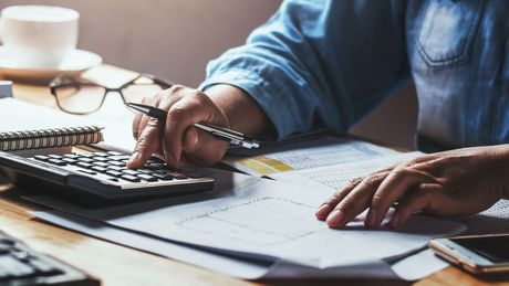 A person is sitting at a desk using a calculator and a pen.