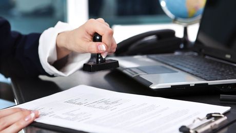 A person is stamping a piece of paper in front of a laptop.