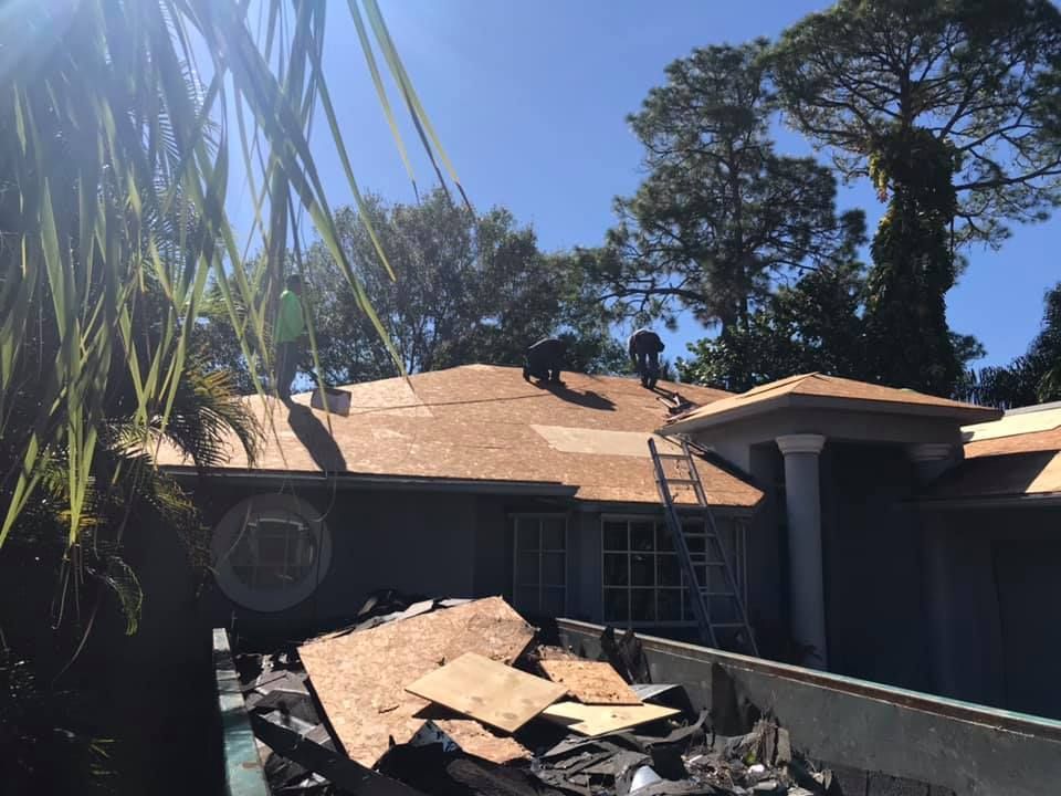 Roofers working on a house under a clear, sunny sky. Debris in a dumpster.