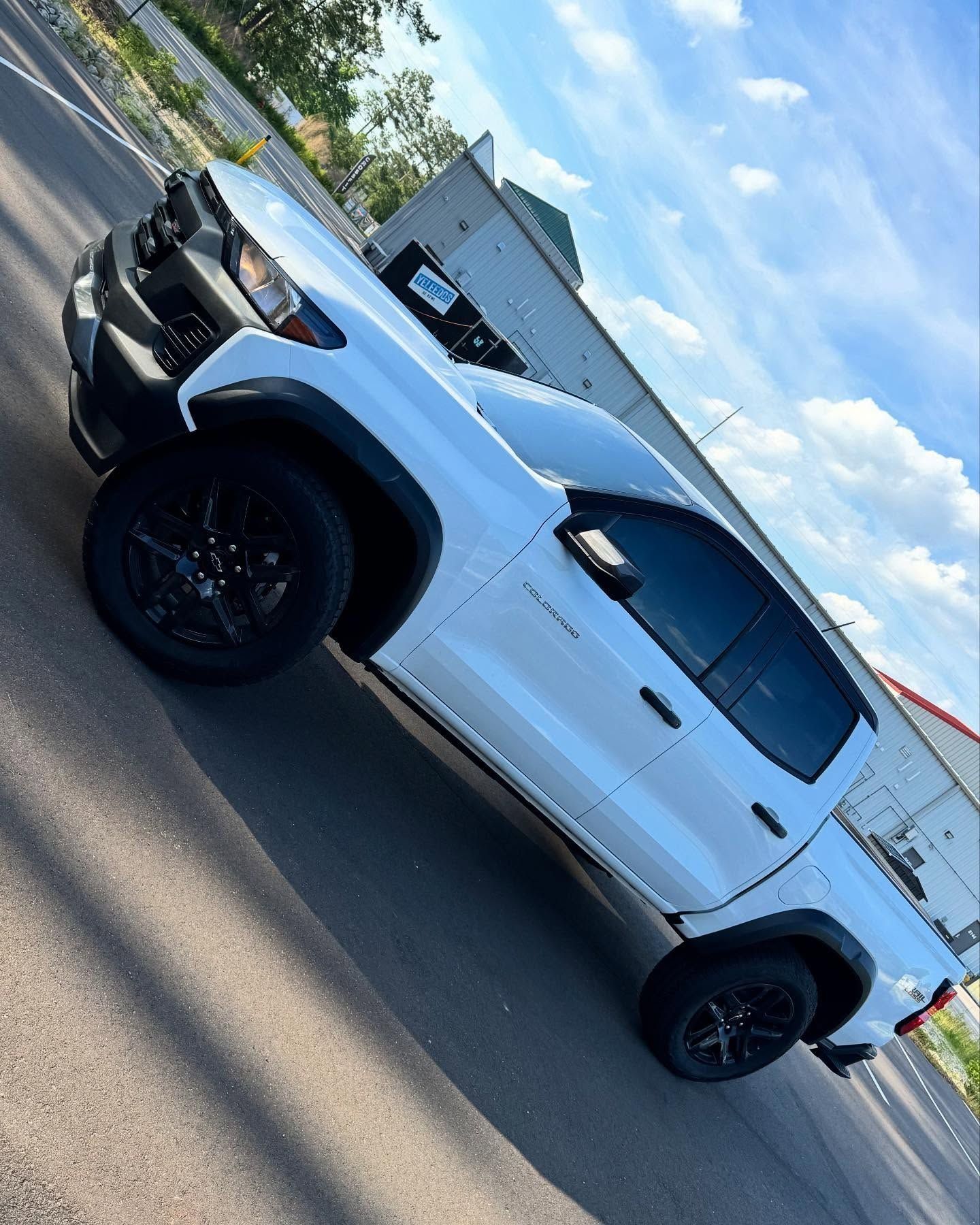 White truck with black accents parked on asphalt. Black wheels and tinted windows. Cloudy sky background.