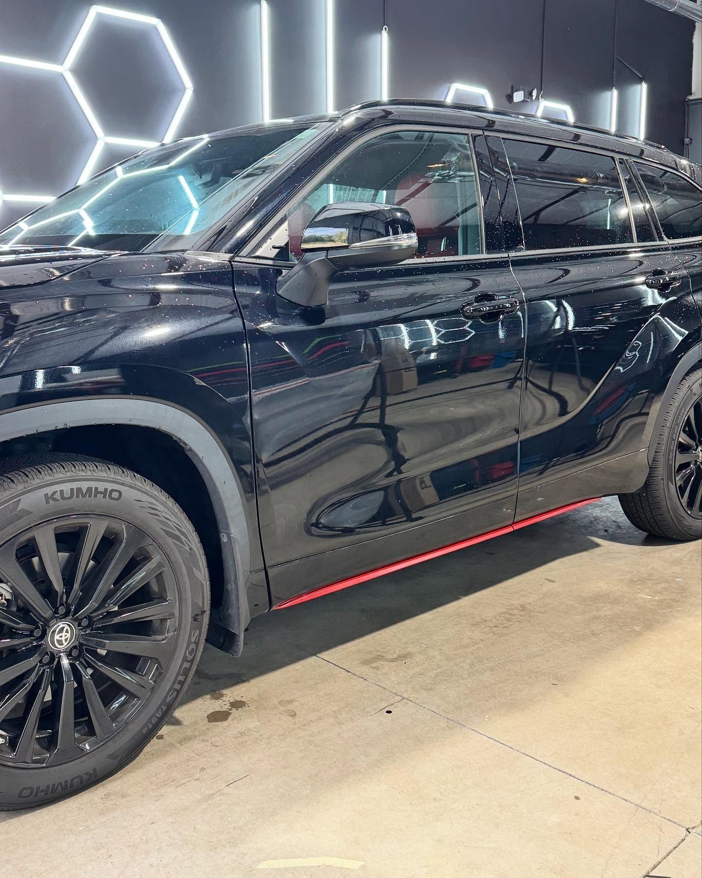Black SUV with black wheels and a red stripe, parked in a car wash bay.