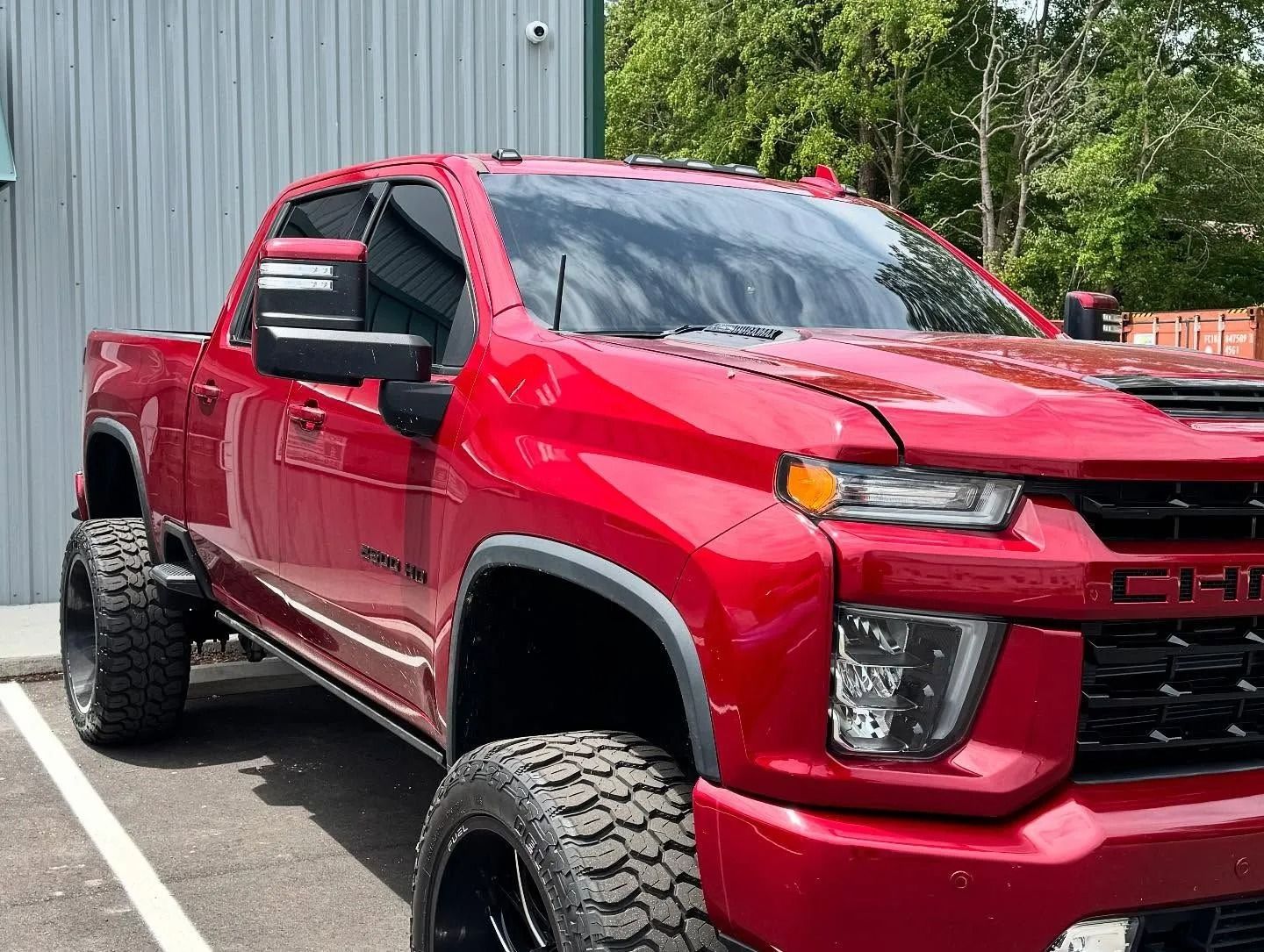 Red Chevrolet pickup truck with large black wheels parked near a building.