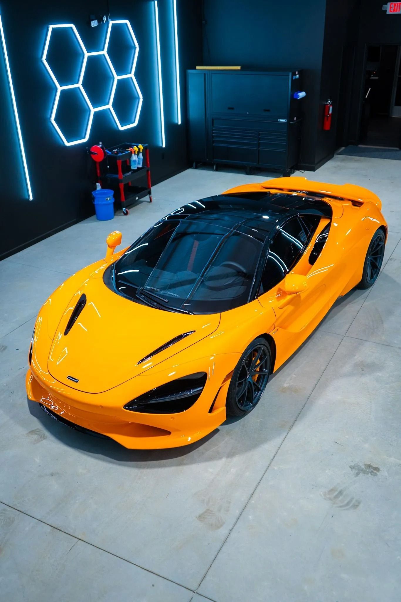 Orange McLaren sports car parked inside a modern garage with neon lights.