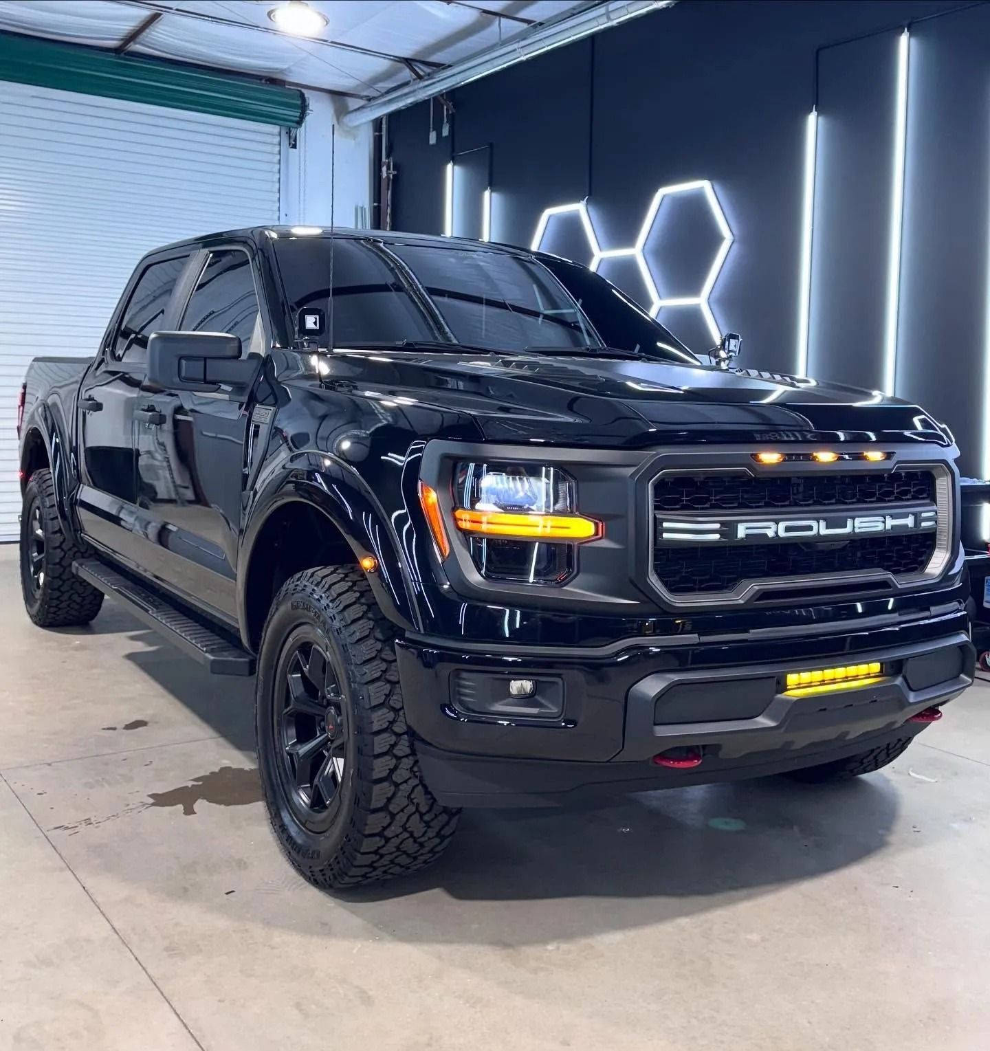 Black Ford truck with tinted windows and black rims in a garage setting.