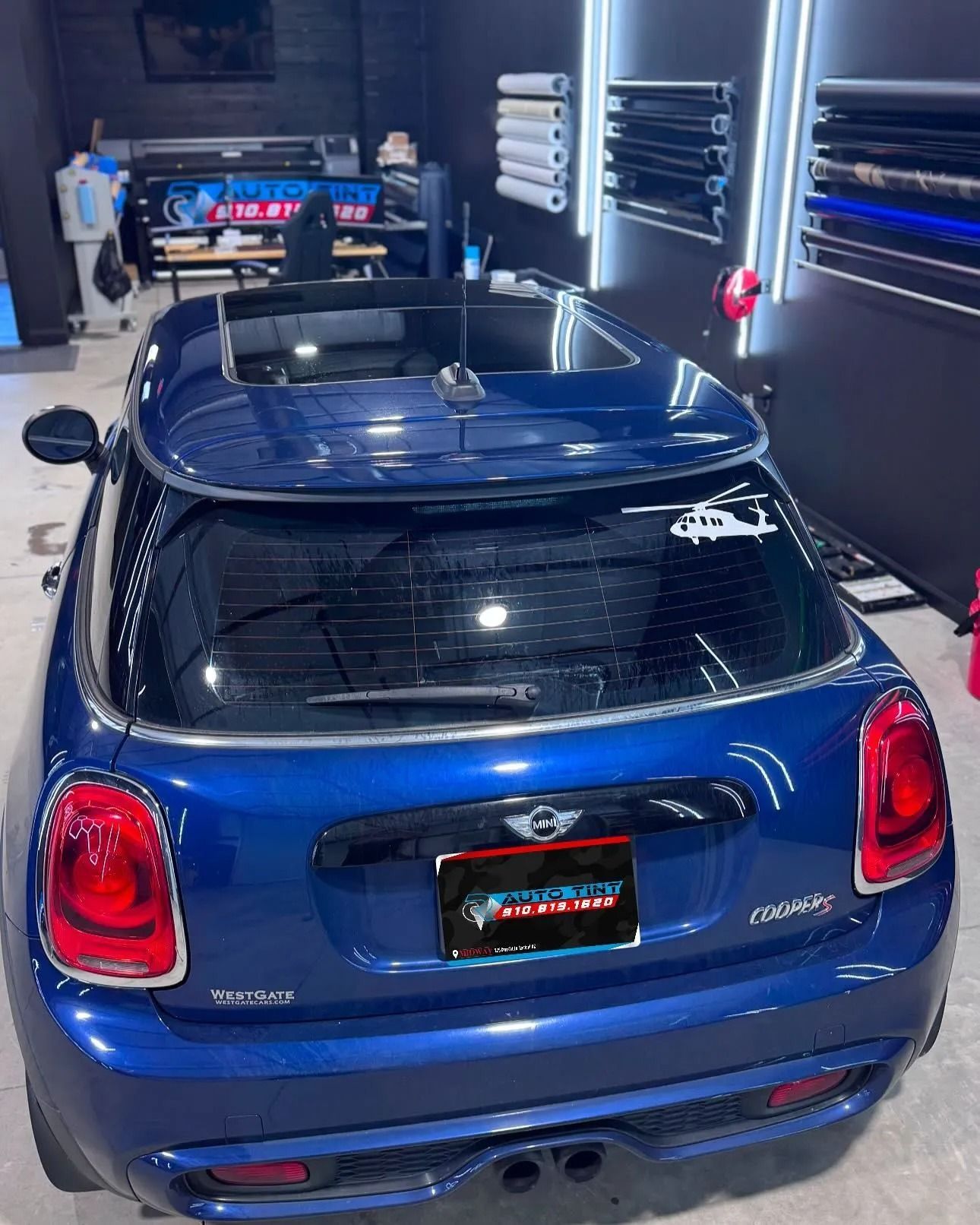 Blue Mini Cooper in a shop with tint film rolls.