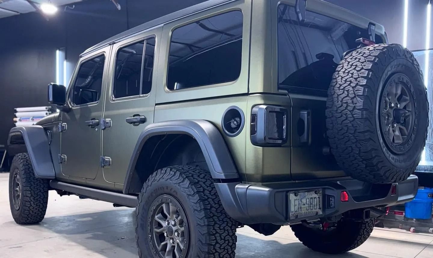 Olive green Jeep Wrangler with black accents and spare tire.
