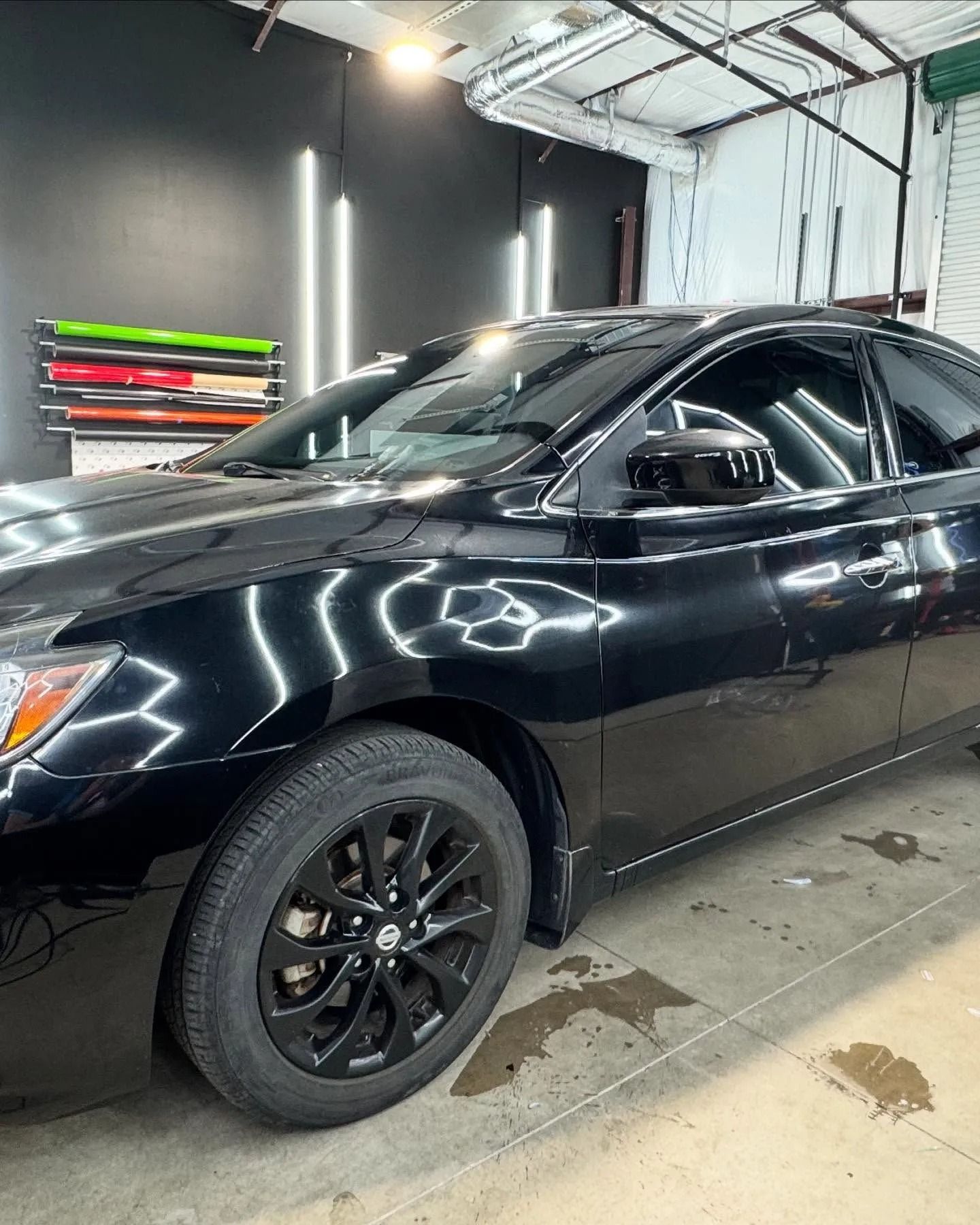 Black car with tinted windows parked in a shop, wheels painted black.