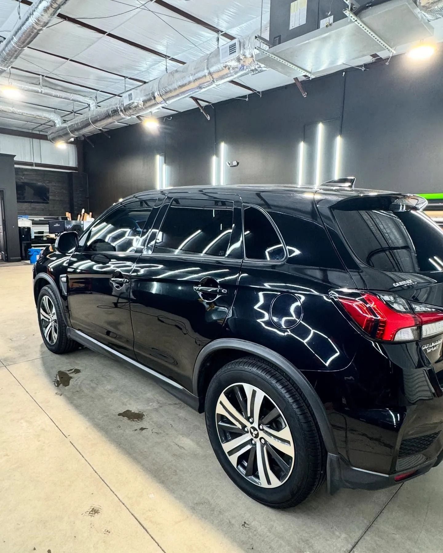 Black SUV parked in a car detailing bay, with reflective surface, tinted windows, and metallic wheels.