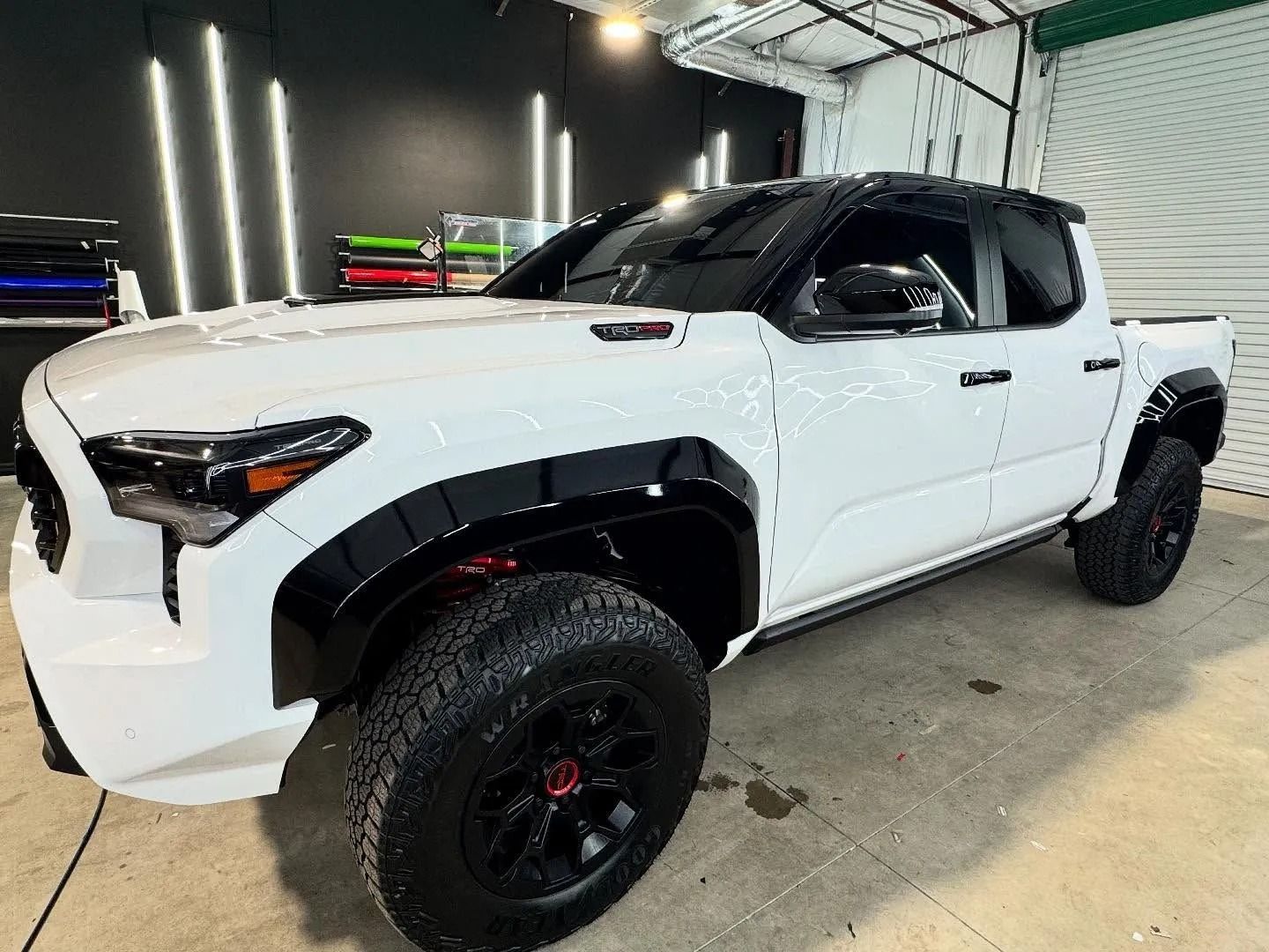 White Toyota Tacoma truck with black accents and large tires parked indoors.