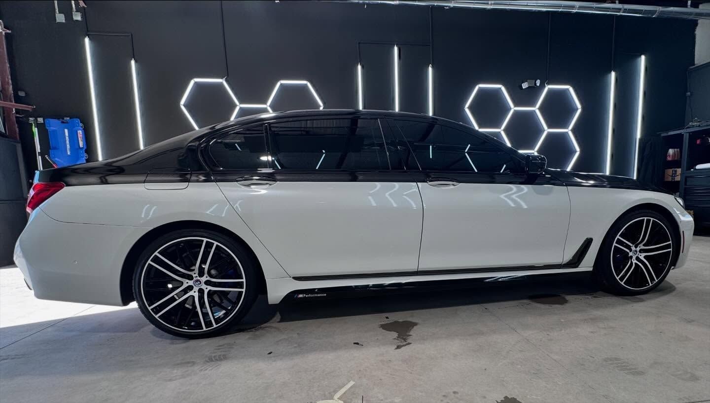 White and black luxury car with tinted windows and black wheels, parked in front of black wall with honeycomb lights.