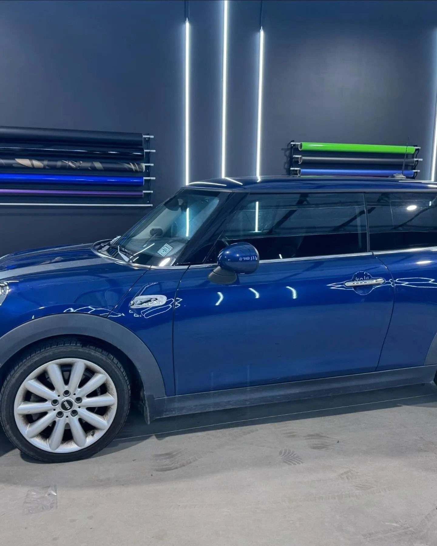 Blue Mini Cooper parked in a shop, rolls of tinted film in the background.