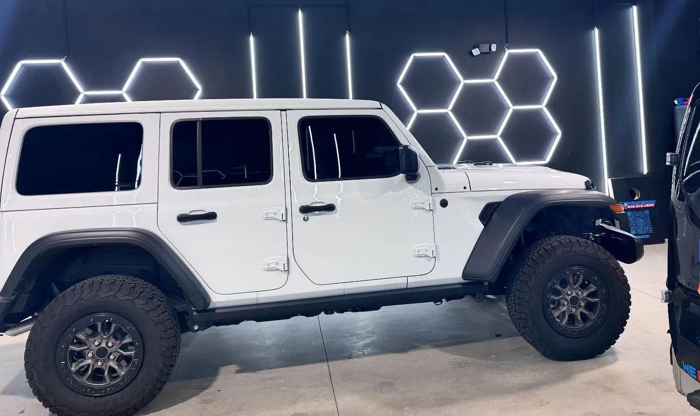 White Jeep with black tires parked inside a garage with hexagon-shaped lights on the wall.