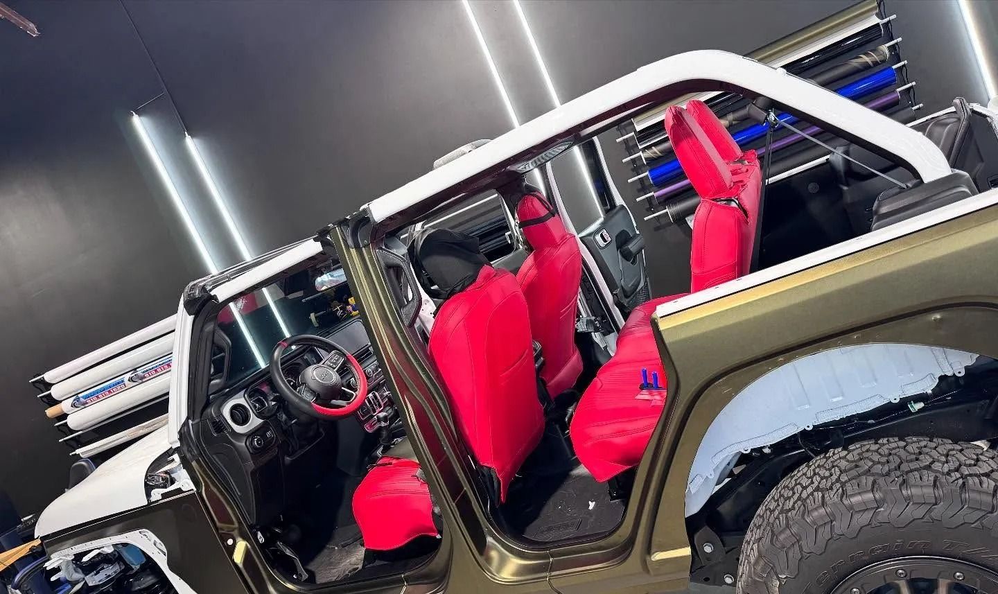 Open-door Jeep with red seats, white top, and black and green exterior, parked in a showroom.