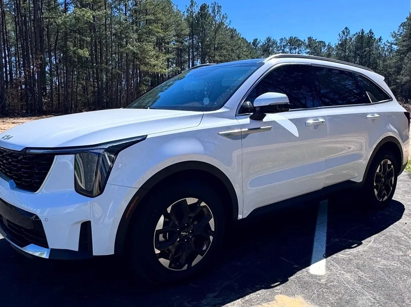 White Kia SUV parked outdoors with black wheels and tinted windows.