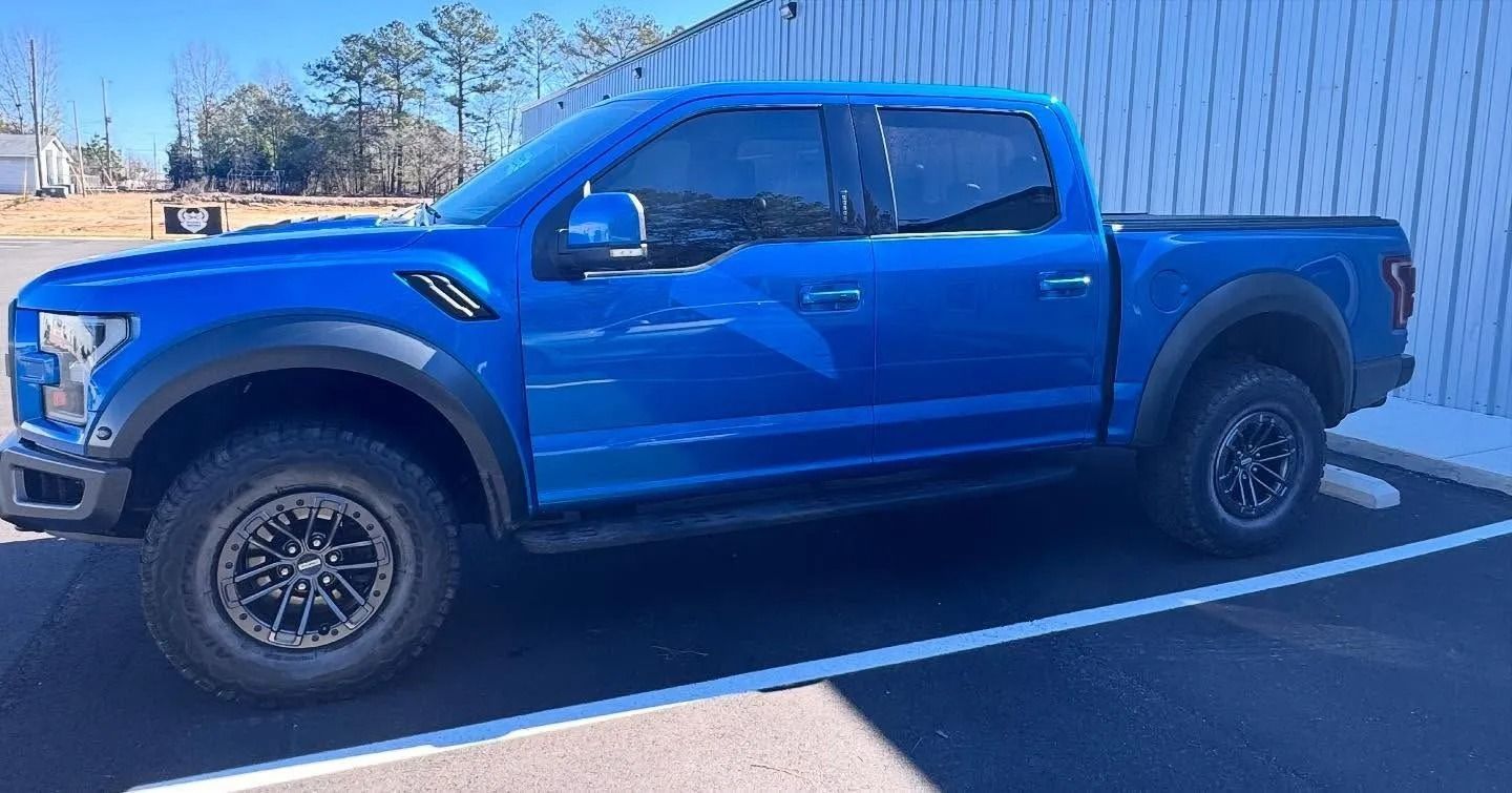Blue Ford Raptor pickup truck parked on pavement.