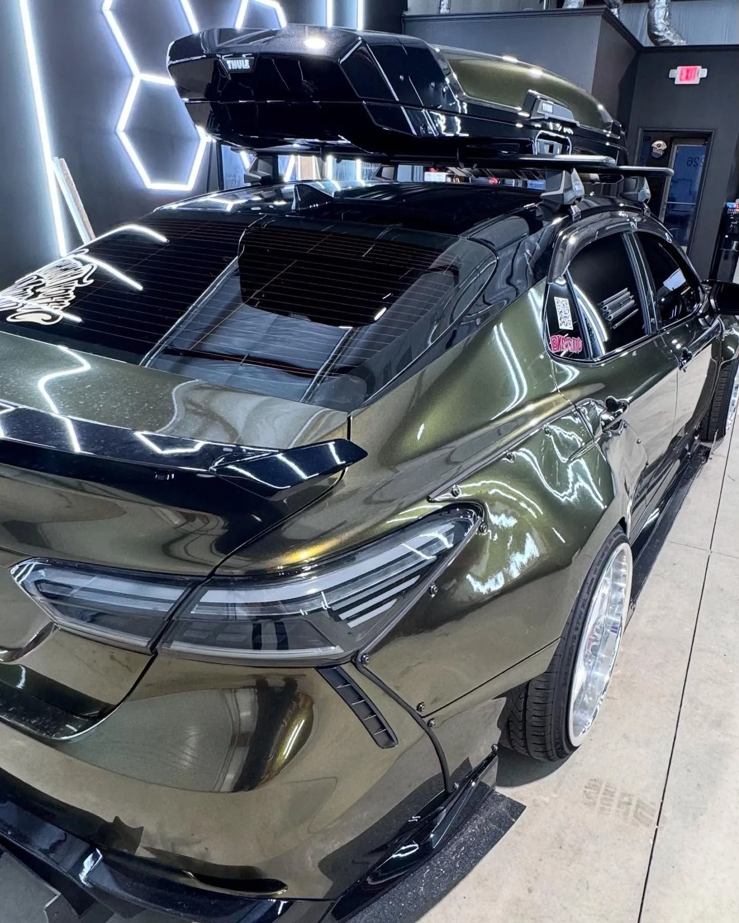 Olive green sedan with roof cargo box, custom bodywork, and low profile tires, parked indoors.