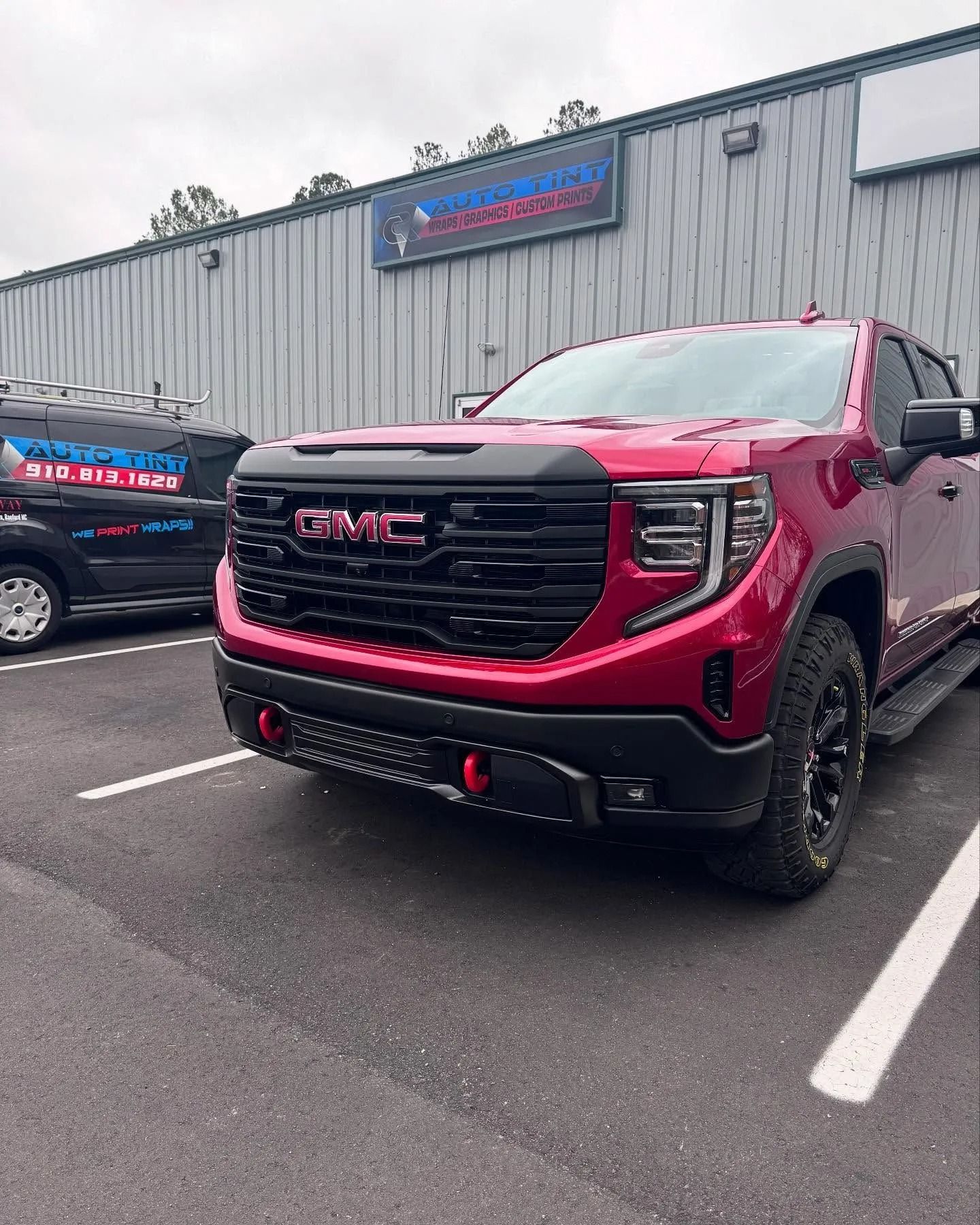 Red GMC Sierra truck parked in front of a building with a business sign.