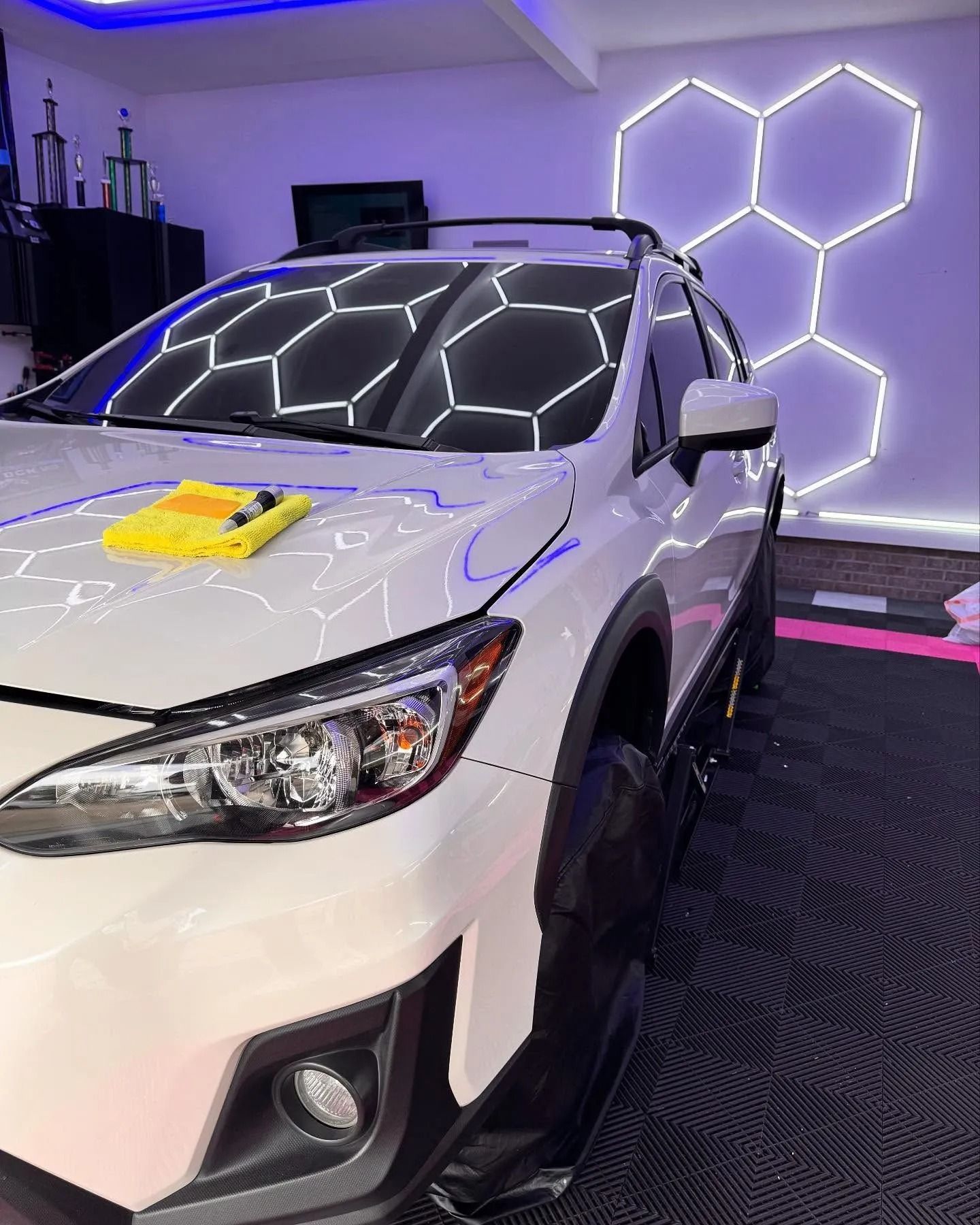 White Subaru car being detailed, with a honeycomb light fixture in the background.