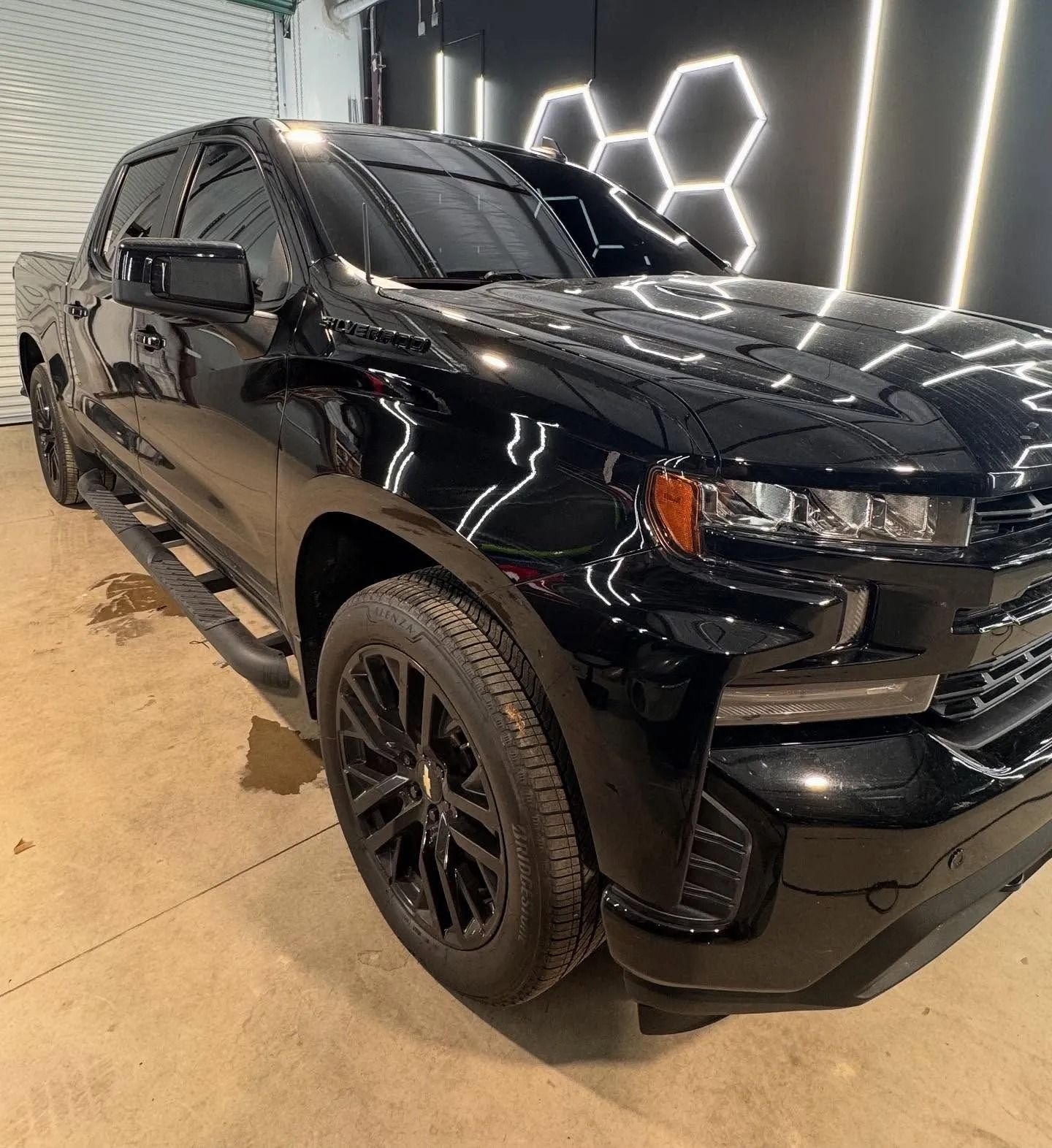 Black Chevy Silverado pickup truck in a garage, with tinted windows and black wheels.