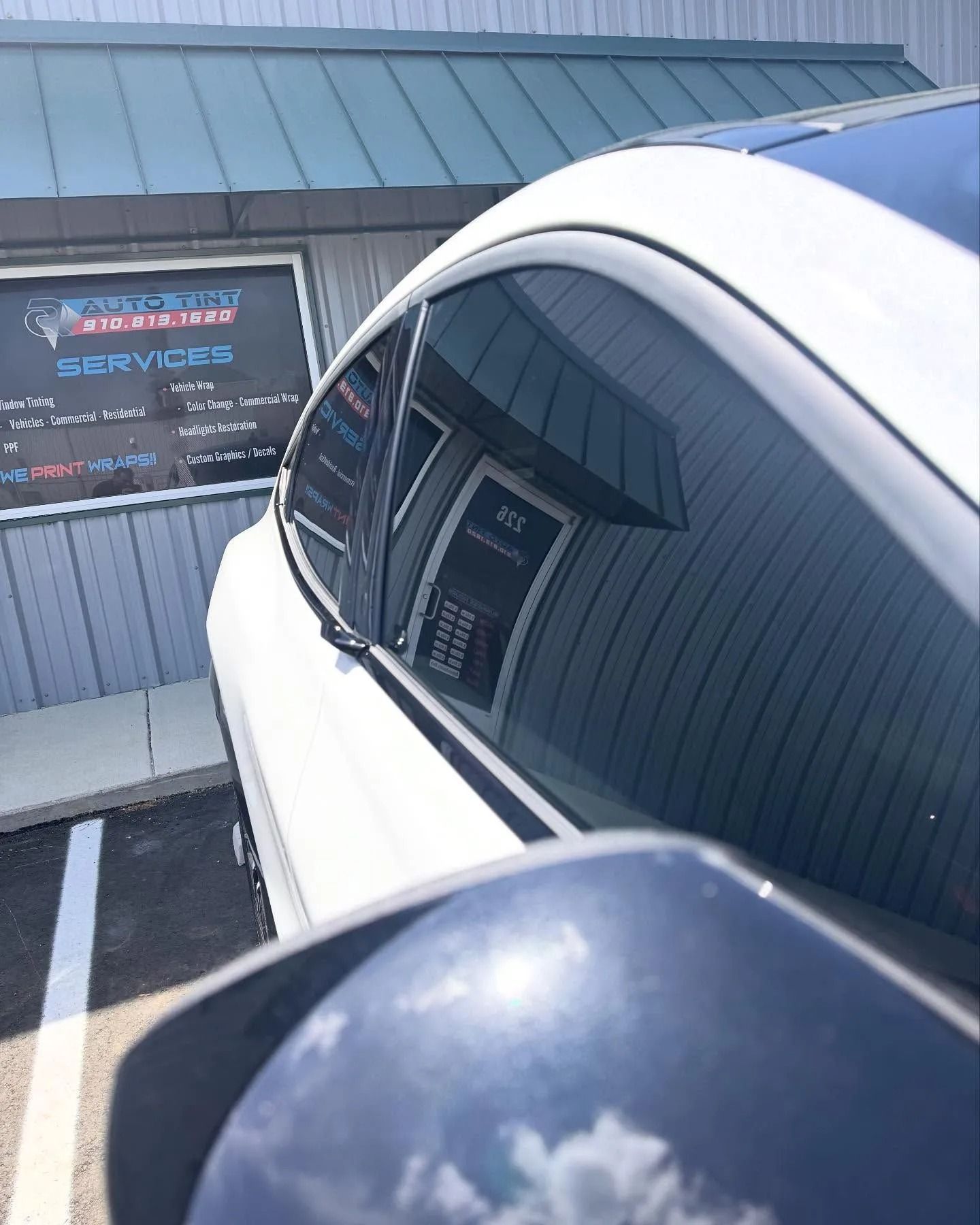 White car parked near a building with a window reflecting the building's entrance.