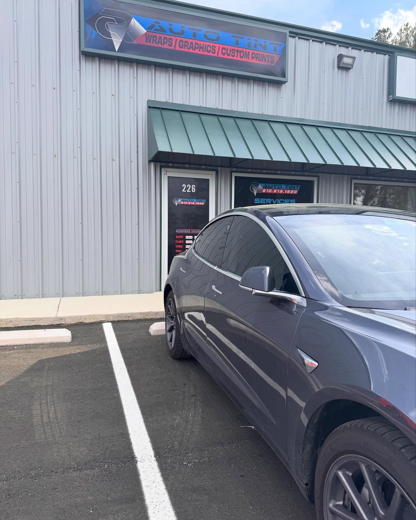 Gray Tesla parked in front of a storefront with a sign, 