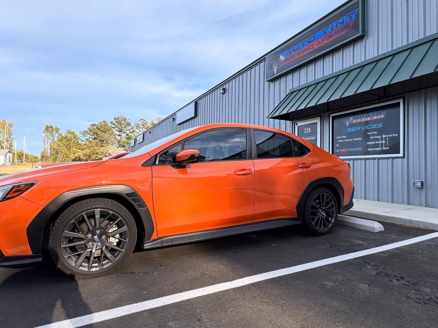 Orange Subaru in front of a blue-gray building with a sign and a green awning.